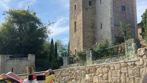 A table with a glass of wine, a bottle, and a bowl of snacks, set against a stone wall with a view of a historic tower. - Luxury apartment in a renovated Chateau with a  view of the Pyrenees. (Mouzens)