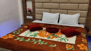 Una cama bien hecha con una colcha estampada de flores, dos almohadas blancas y dos almohadas decorativas rojas.