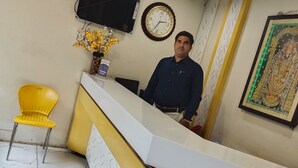 Un área de recepción con mostrador, una silla amarilla, un reloj y un televisor en la pared.