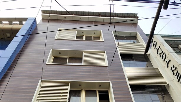 Un edificio de varios pisos con fachada moderna, que presenta ventanas rectangulares con persianas, una entrada visible con un letrero decorativo y un cartel con la dirección a la vista.