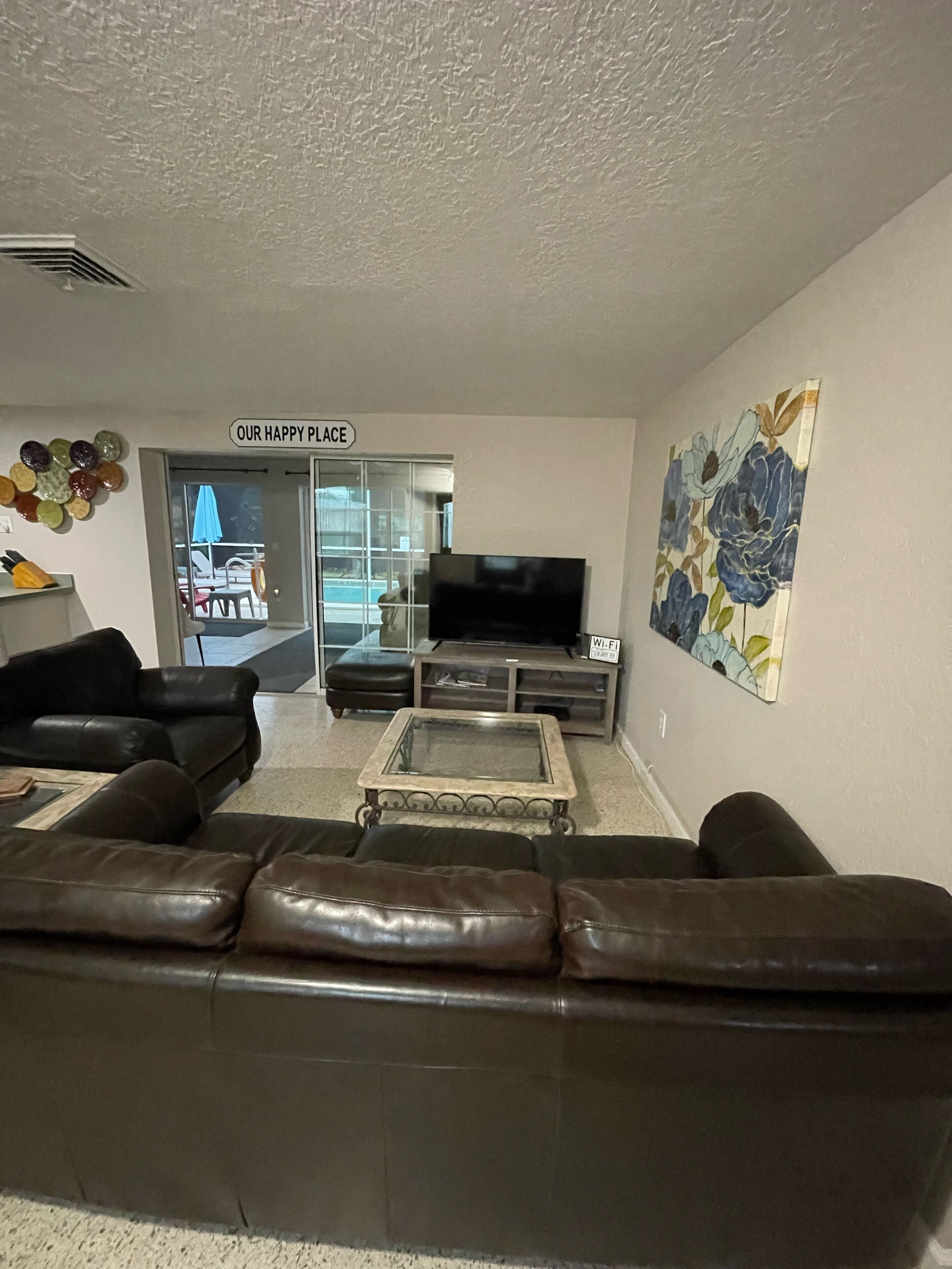 A living room with a leather sofa, a glass coffee table, a flat-screen TV, and a floral artwork on the wall.