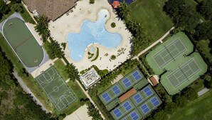 Vista aérea de un complejo deportivo con varias canchas de tenis, una piscina y una cancha de baloncesto.