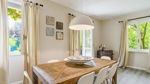 A dining area with a wooden table, white chairs, a hanging light fixture, and artwork on the walls. - Bright and welcoming two-level villa with large garden, just 5km from Bellagio and 2.5km from the pretty village of Civenna! The villa is located halfway between the picturesque Bellagio (a stunning town on the Como Lake) and Mount S.Primo, which offers  (Gallasco-cernobbio)