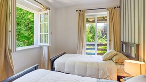A bedroom with two beds, a window with curtains, a view of greenery, and a striped wall. - Bright and welcoming two-level villa with large garden, just 5km from Bellagio and 2.5km from the pretty village of Civenna! The villa is located halfway between the picturesque Bellagio (a stunning town on the Como Lake) and Mount S.Primo, which offers  (Gallasco-cernobbio)