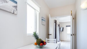 A clean, white dining area with a bowl of fruit on the table, a white chair, and a view of a hallway leading to another room. - Mariners (5) - Bright and stylish apartment - 2-minute walk to the beach (Luz)
