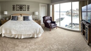 A bedroom with a large bed, a leather chair, a TV, and a view of a body of water. - Spectacular waterfront luxury (Village of Four Seasons)