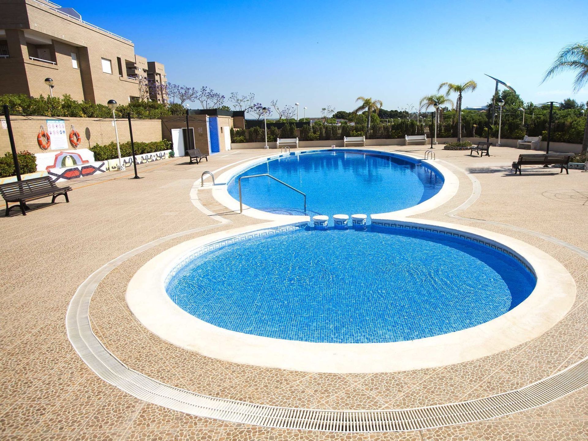 A large, circular swimming pool with a tiled edge, surrounded by a pebble-patterned deck.
