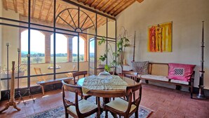 Uma área de refeições com mesa e cadeiras, um sofá e vista através de grandes janelas.