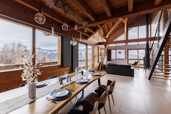 Enjoy meals in this dining area with a long table and views of the surrounding mountains and trees.