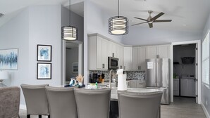 A modern kitchen with white cabinets, stainless steel appliances, and a bar area with four chairs. - Modern 4BR Beach House | Pool, Walk to Beach & Prime Location (Fort Myers Beach)