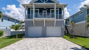 A two-story house with a balcony, two garages, and a paved driveway. - Modern 4BR Beach House | Pool, Walk to Beach & Prime Location (Fort Myers Beach)