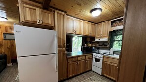 A compact kitchen with wooden cabinets, a white refrigerator, a stove, and a microwave. - Cardinal's Landing-Covered Porch - Pet-Friendly - Private-4WD-AWD (Bryson City)