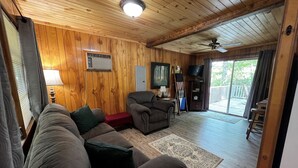 A cozy living room with wooden walls and ceiling, a sofa, a chair, a TV, and a balcony with a view. - Cardinal's Landing-Covered Porch - Pet-Friendly - Private-4WD-AWD (Bryson City)