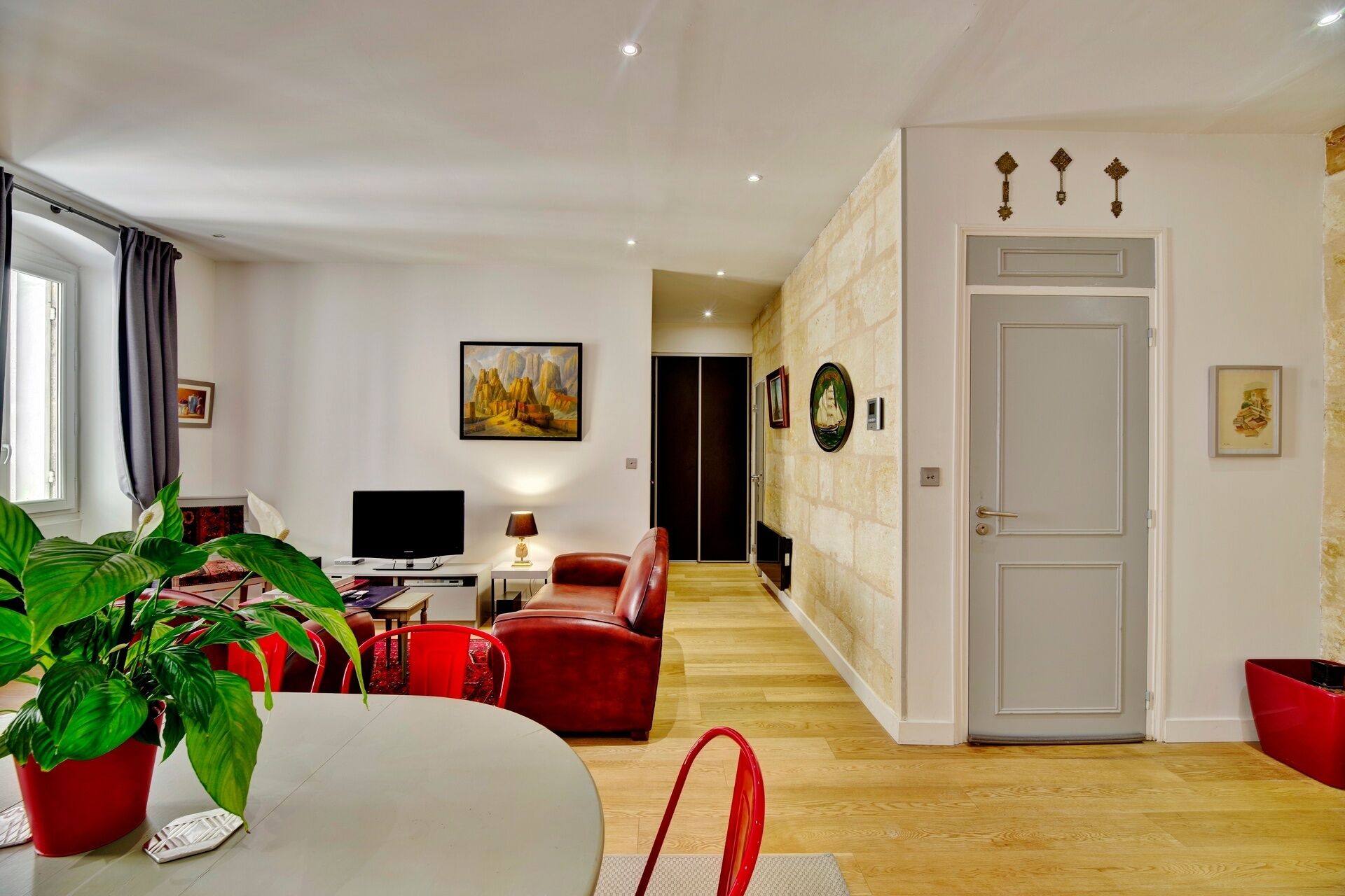 A modern living room with a TV, red leather sofa, and a dining table with a potted plant.