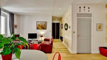 A modern living room with a TV, red leather sofa, and a dining table with a potted plant.