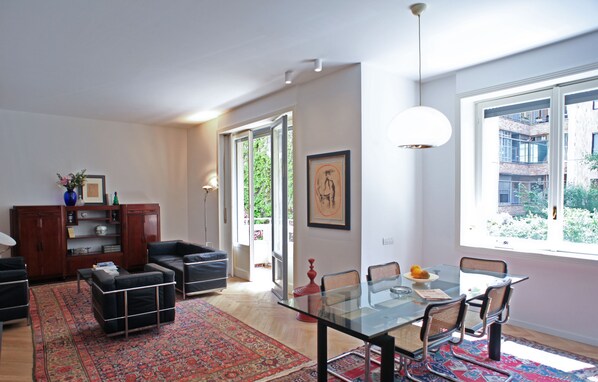 A modern living room with a glass dining table, leather sofas, and a red patterned rug.