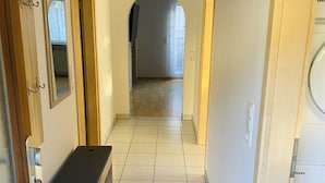 Un pasillo con un banco, una lavadora y una puerta con un espejo.
