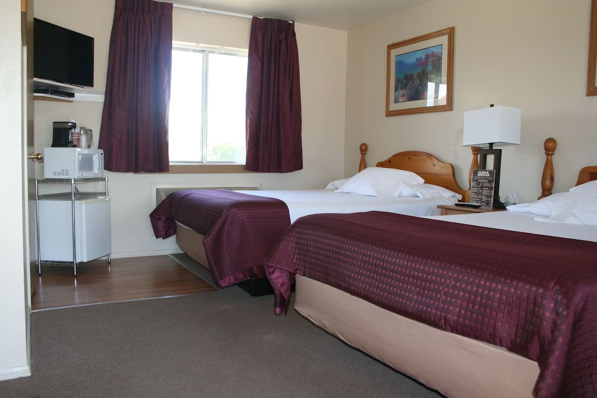 A hotel room with two beds, a desk with a microwave, a TV, and a painting on the wall.