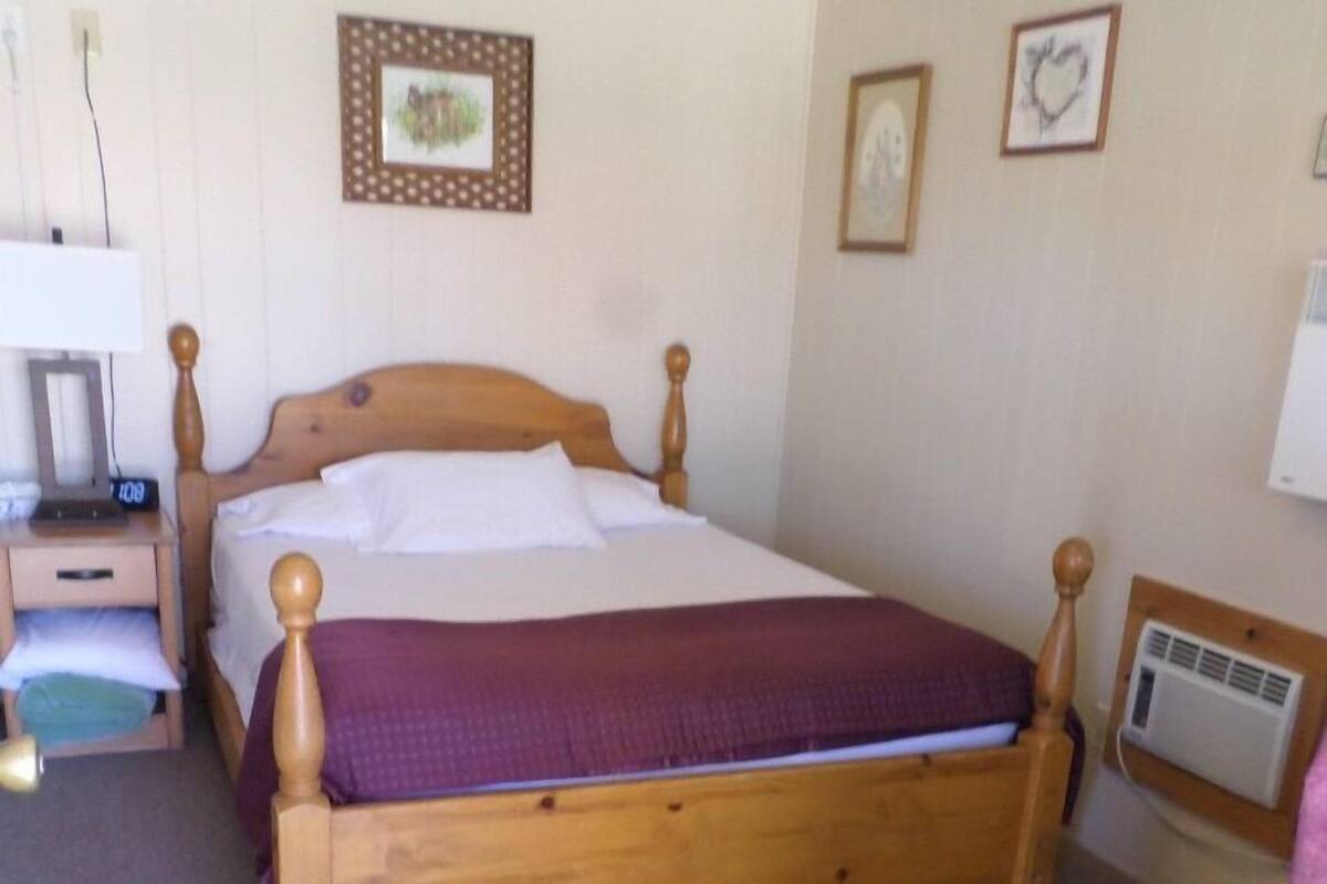 A single-bed room with a wooden headboard, a bedside table with a lamp, and a small dresser.