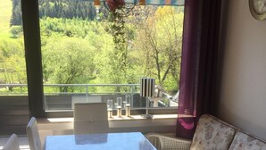 Ein Essbereich mit Tisch und Stühlen, einer Couch und Blick auf Grün durch große Fenster.