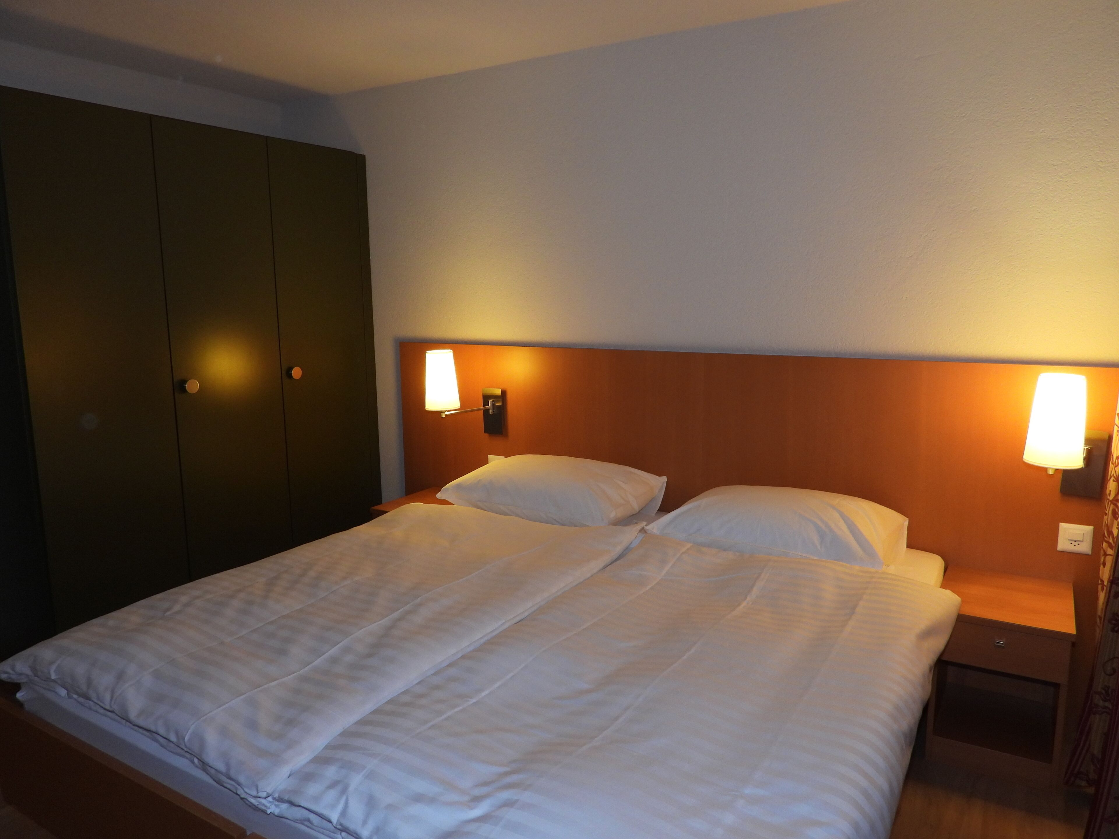 Ein Doppelbett mit weißen Leinen, ein Holz-Kopfteil und zwei Nachttische mit Lampen.
