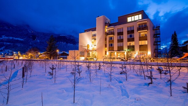 A modern hotel with multiple floors, a prominent entrance, and a snow-covered landscape in the foreground. - Hotel Sherlock Holmes "nur 200 m zur Gondelbahn Hasliberg" (Meiringen)