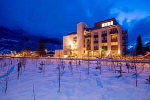 Un hôtel moderne à plusieurs étages, doté d’une entrée imposante et surplombant un paysage enneigé.