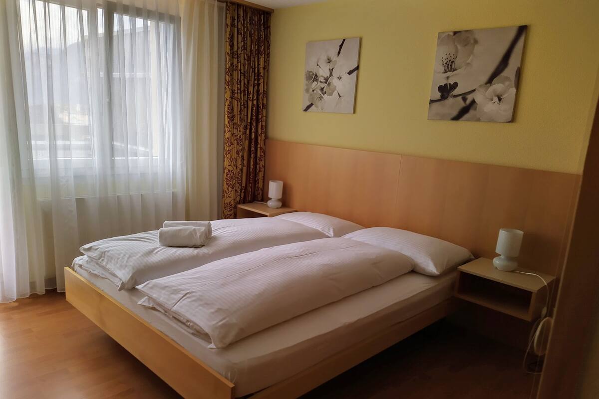 A hotel room with a double bed, two bedside tables, a nightstand, and two wall-mounted paintings.