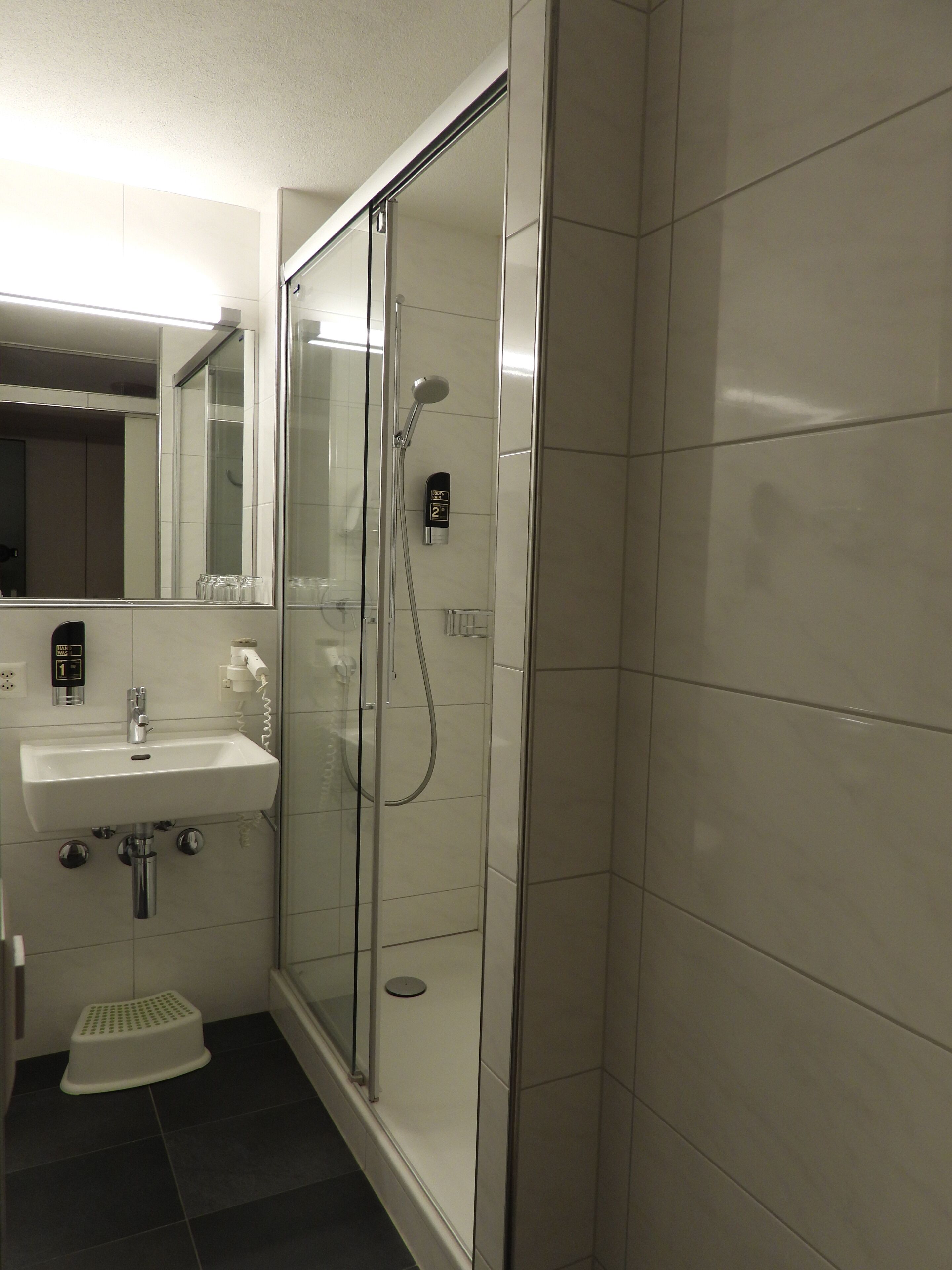 Une salle de bain moderne avec une douche à parois de verre, un lavabo avec un miroir et un petit tabouret.