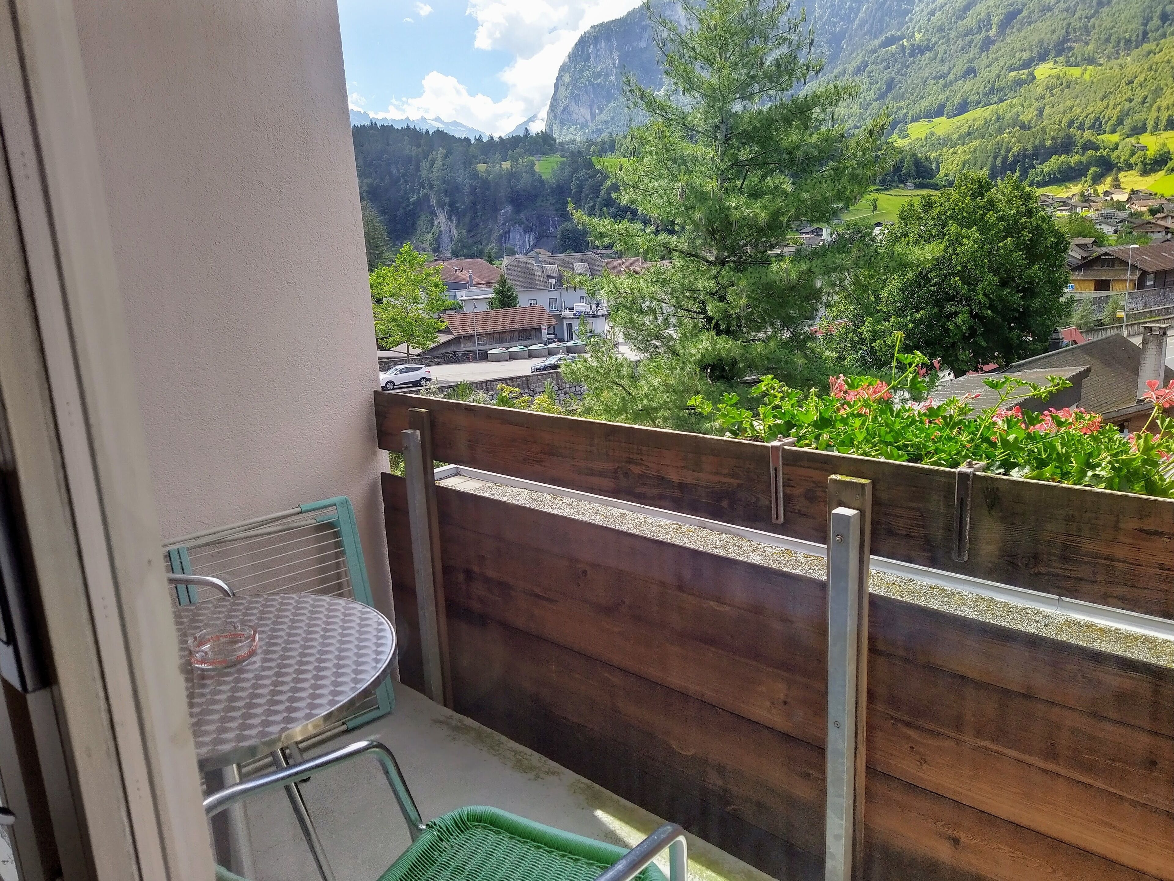 A balcony with a view of a mountainous landscape, a wooden fence, and a small table with a chair.