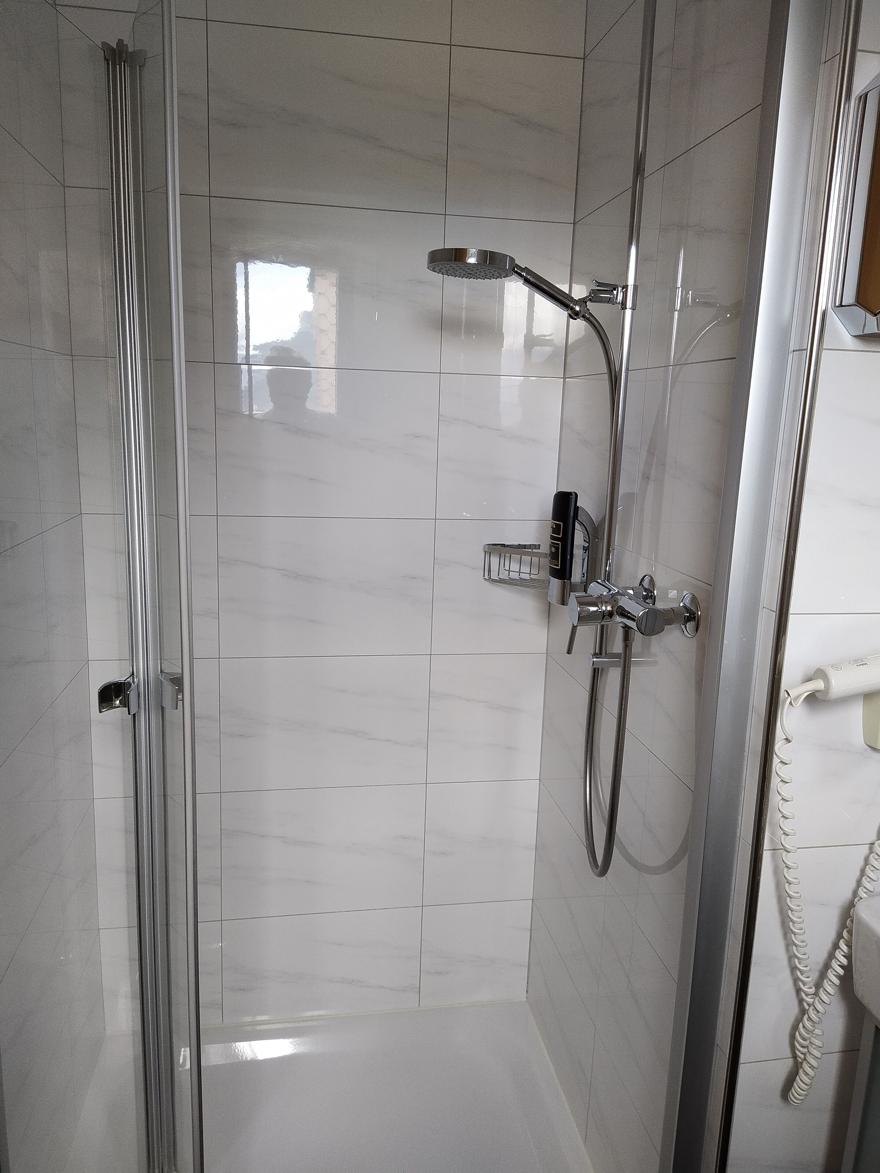 Un baño moderno con cabina de ducha de vidrio, ducha con cabezal de mano y grifo empotrado en la pared.