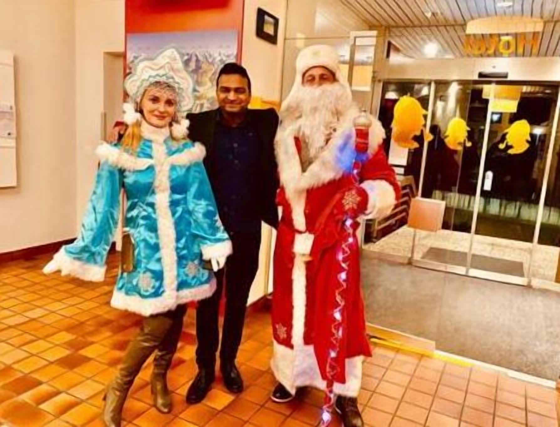A person in a Santa Claus costume standing next to a person in a blue dress and another person in a suit.