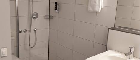 A modern bathroom with a glass-enclosed shower, a white sink, and a towel rack.