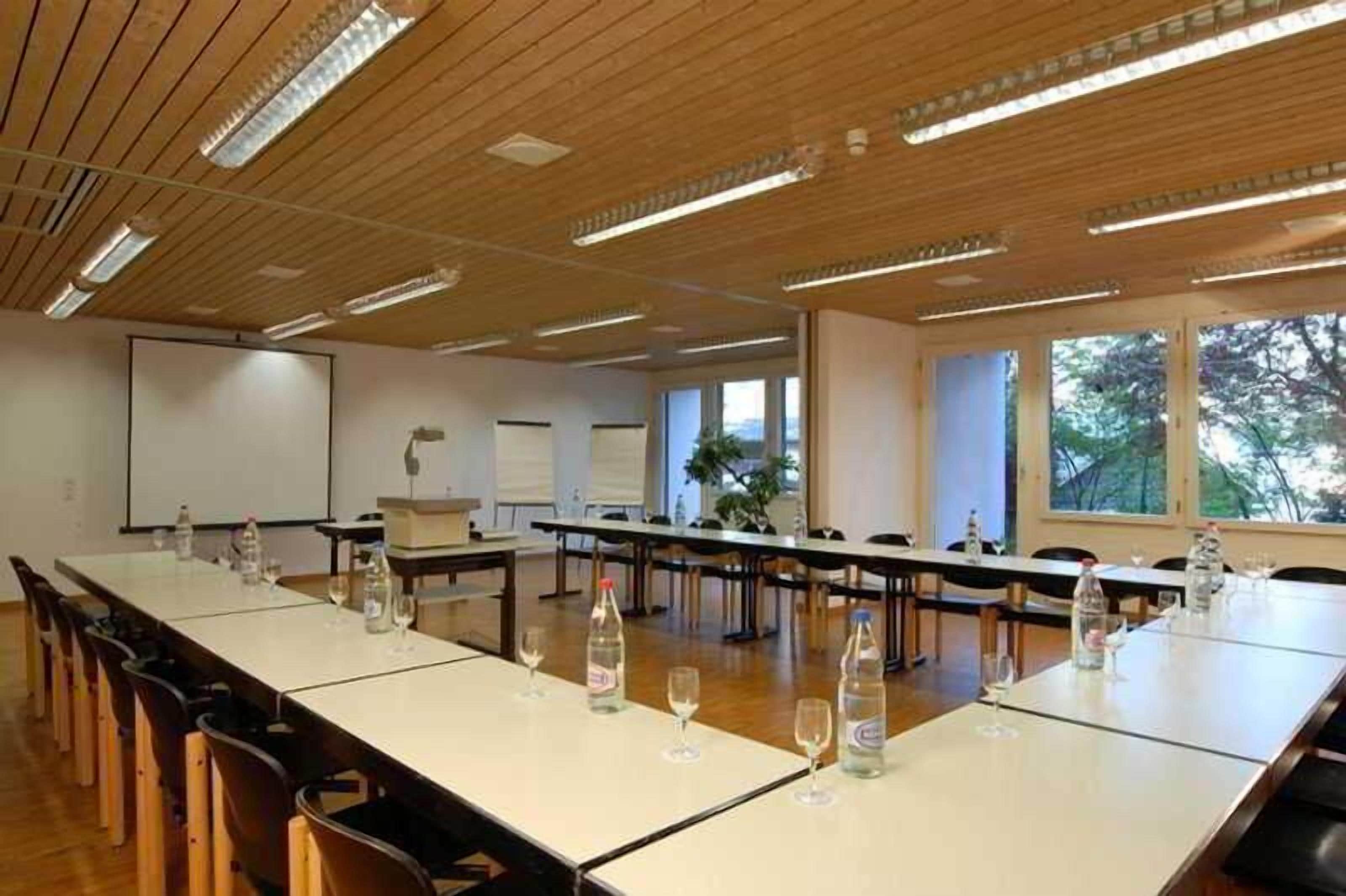 A conference room with long tables, chairs, and a projector screen.