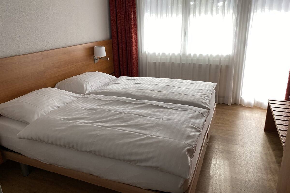 A double bed with white linens in a hotel room.