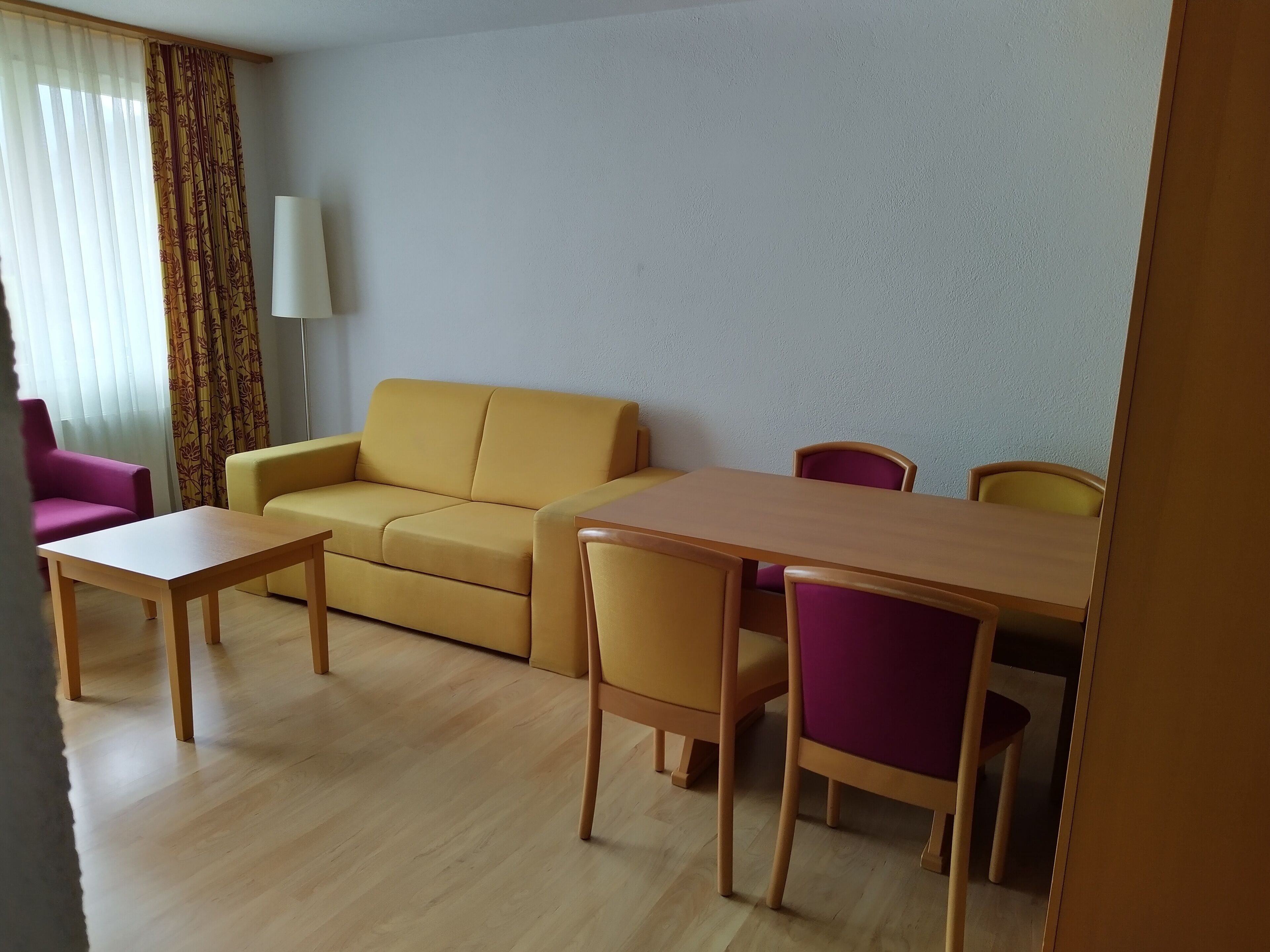 Una sala de estar con un sofá amarillo, una mesa de centro de madera y sillas moradas.