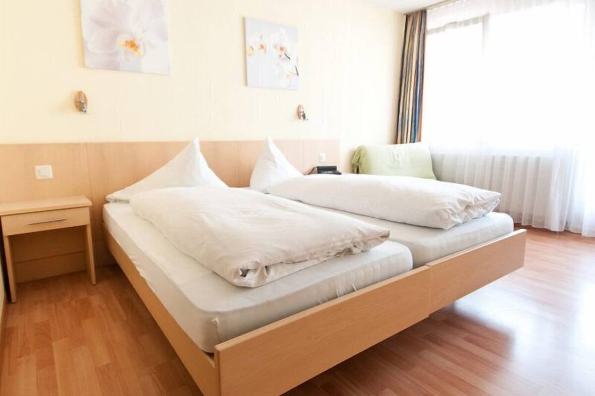 A double bed with white bedding in a room with wooden flooring and a nightstand.