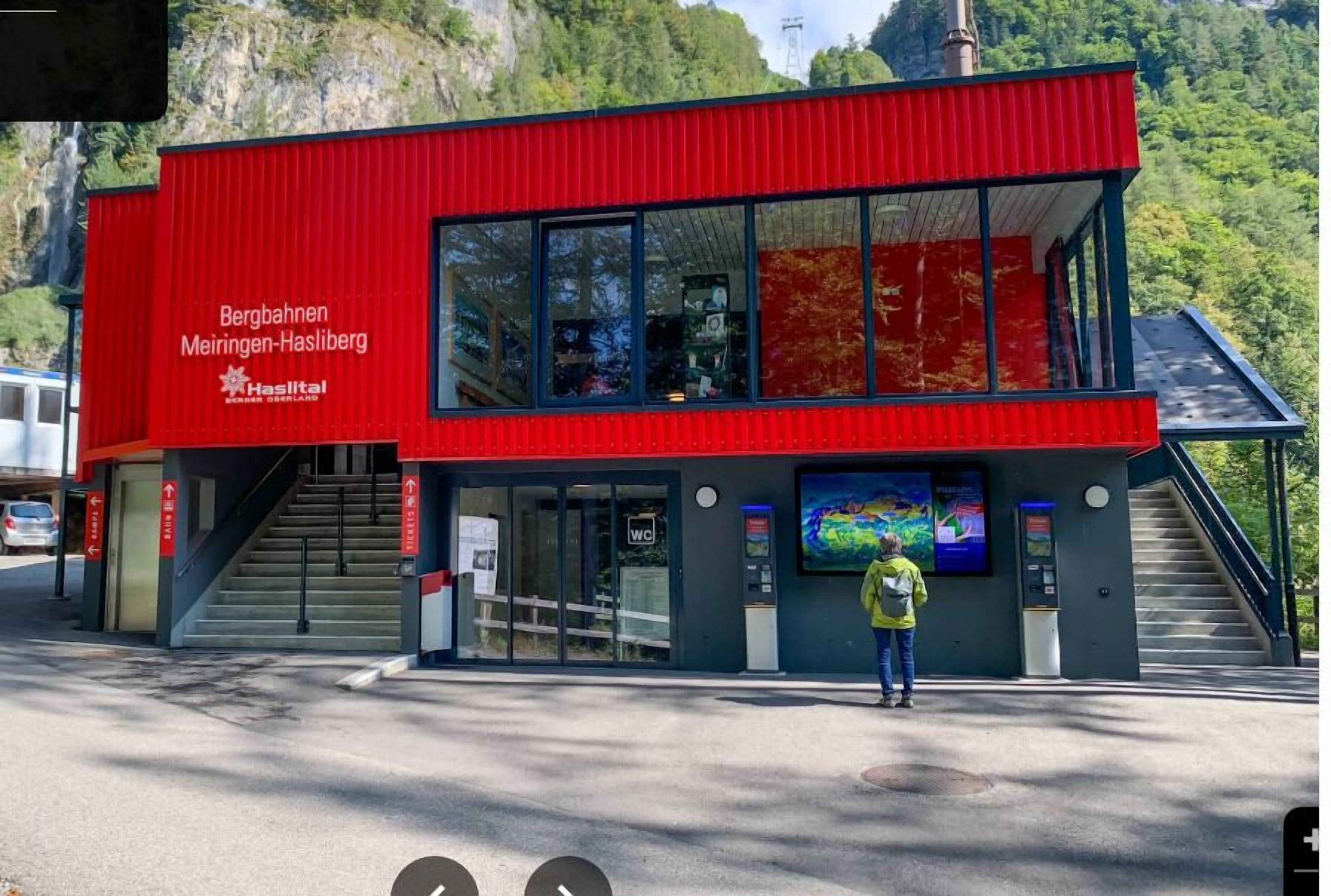 Un bâtiment moderne de couleur rouge, doté de grandes fenêtres en verre et d’un escalier menant à l’entrée.
