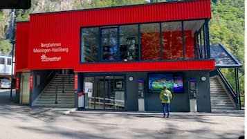 Un bâtiment moderne de couleur rouge, doté de grandes fenêtres en verre et d’un escalier menant à l’entrée.