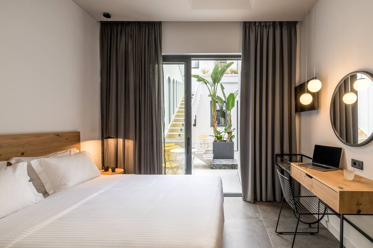 A modern hotel room with a bed, a desk, and a view of the outside.