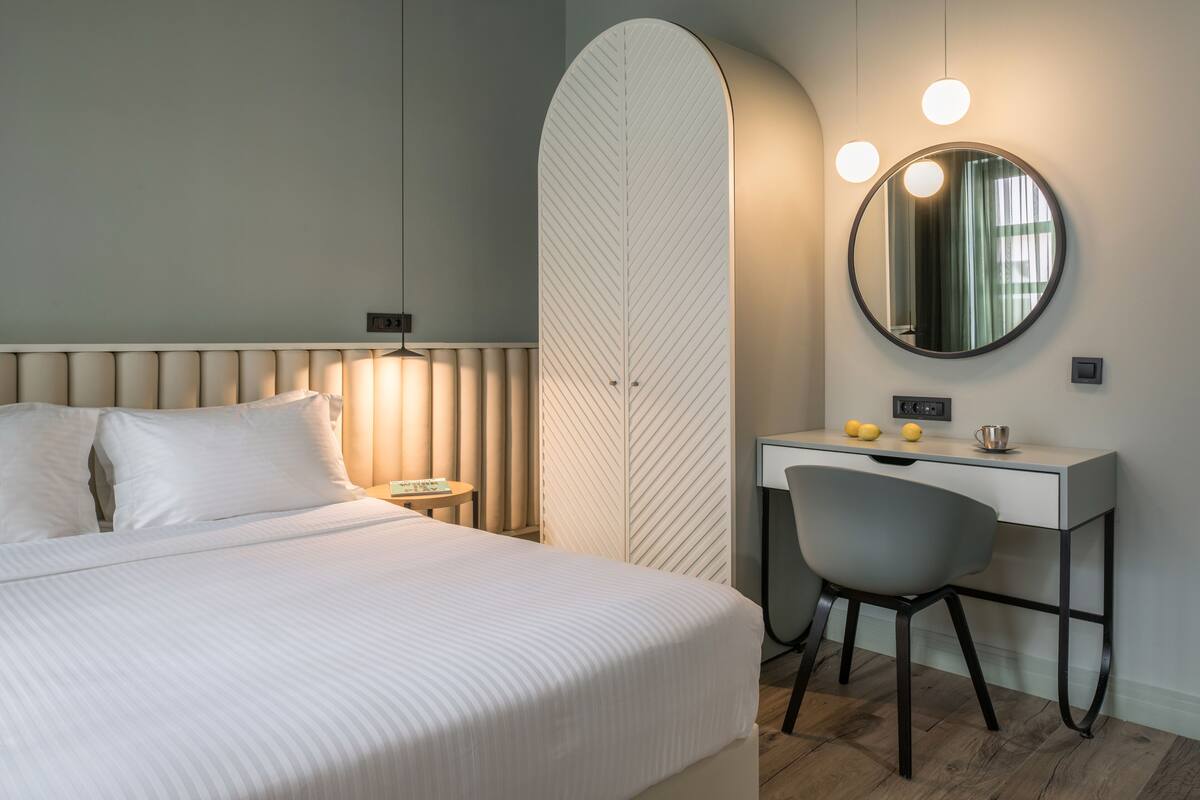 A modern hotel room with a large bed, a desk with a chair, a round mirror, and a unique leaf-shaped partition.