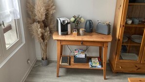 Une table en bois avec une machine à café, une bouilloire et un grille-pain, un vase contenant de l’herbe des pampas et un buffet rempli de vaisselle.