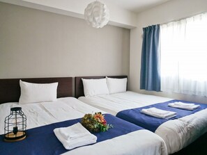 Et hotelværelse med to senge, en moderne lysekrone, et vindue med gardiner og et lille bord med lampe og blomster.