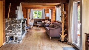 Een gezellig cabin interieur met een stenen open haard, houten vloeren, een bank en een groot raam.