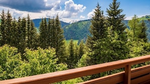 Een houten balkonhek met uitzicht op een bebost berglandschap onder een heldere lucht.