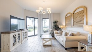 A modern living room with a flat-screen TV, a chandelier, a sofa set, and a wooden cabinet.