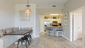 A modern kitchen with white cabinets, a central island, and a dining area with a wooden table and metal chairs.