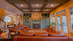 A spacious living room with a large leather sofa, a fireplace, and a view of the outdoors through large windows. - Lakefront Exclusive French Tudor Castle. 8400 sf. Nicest property on SML!  (Penhook)