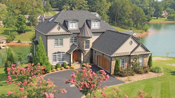 A large, two-story house with a stone facade, a large garage, and a driveway leading to a lake. - Lakefront Exclusive French Tudor Castle. 8400 sf. Nicest property on SML!  (Penhook)