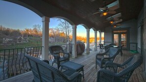 A covered outdoor deck with wicker furniture, a grill, and a view of a lake and trees. - Lakefront Exclusive French Tudor Castle. 8400 sf. Nicest property on SML!  (Penhook)